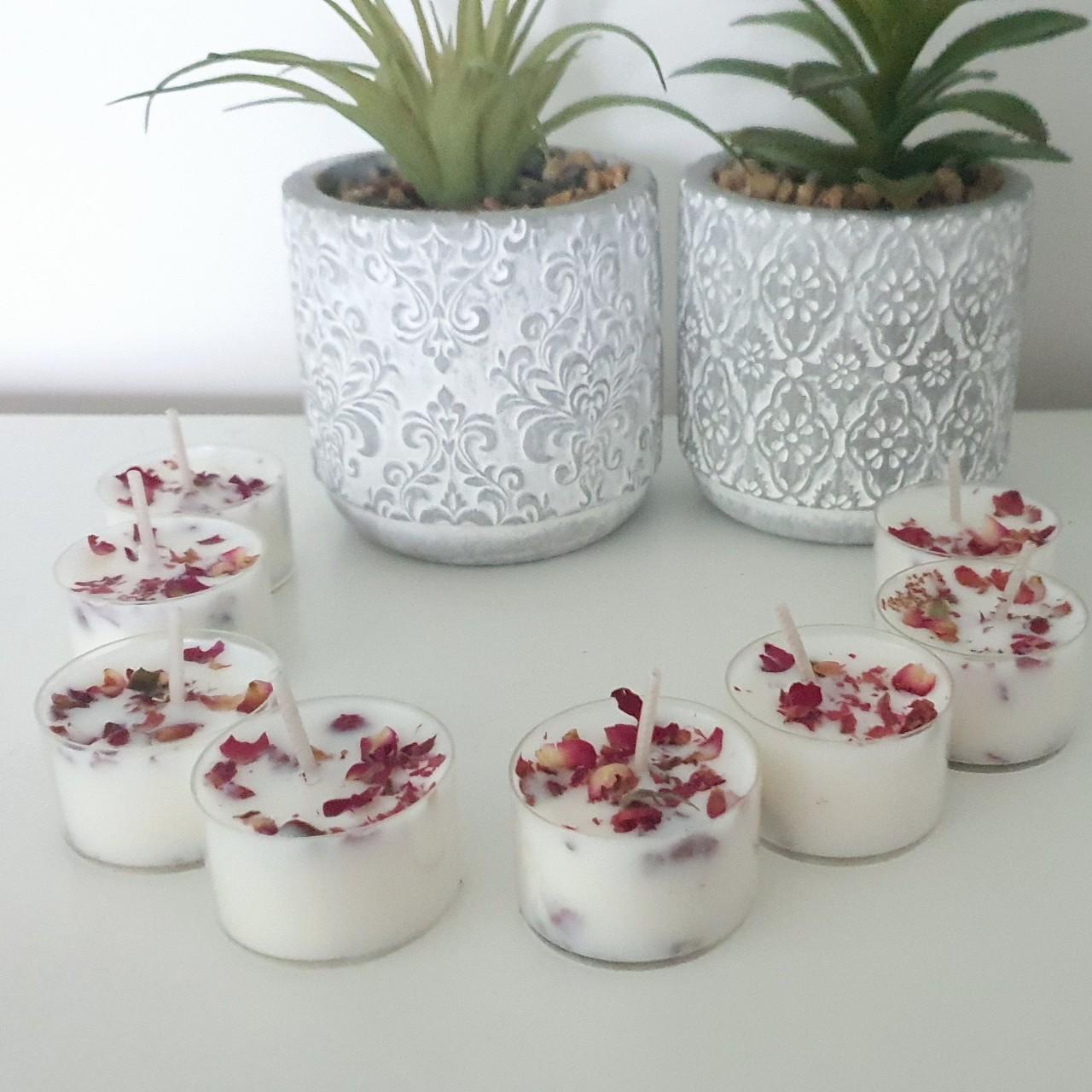 Votive candles with rose petals in front of decorative pots on a white surface